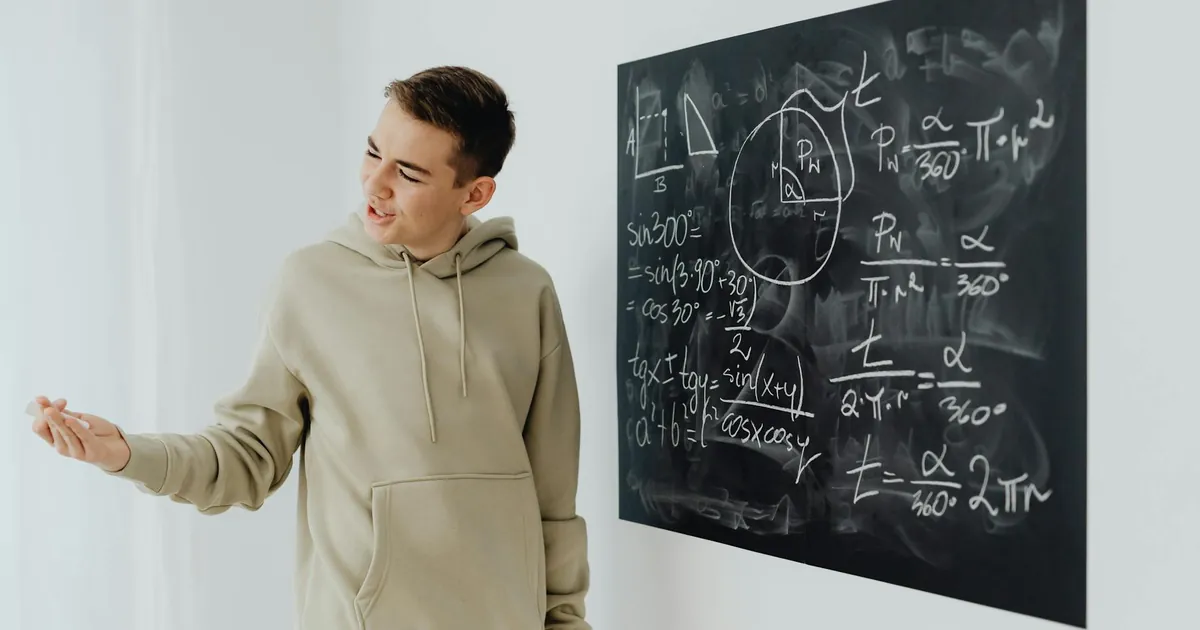 Enthusiastic teen boy in a hoodie teaching math on a blackboard.