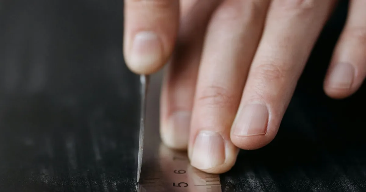Macro shot of fingers precisely using a stainless steel ruler on a dark surface.