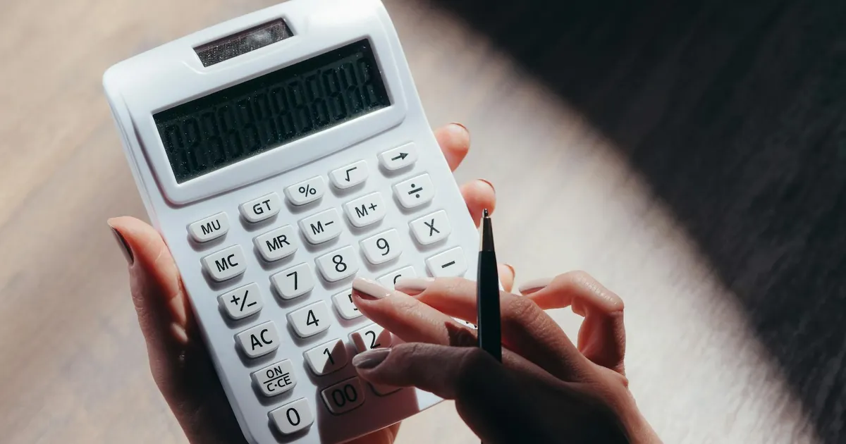 Hands holding a calculator and pen for financial calculations in a well-lit setting. Hands holding a calculator and pen for financial calculations in a well-lit setting.