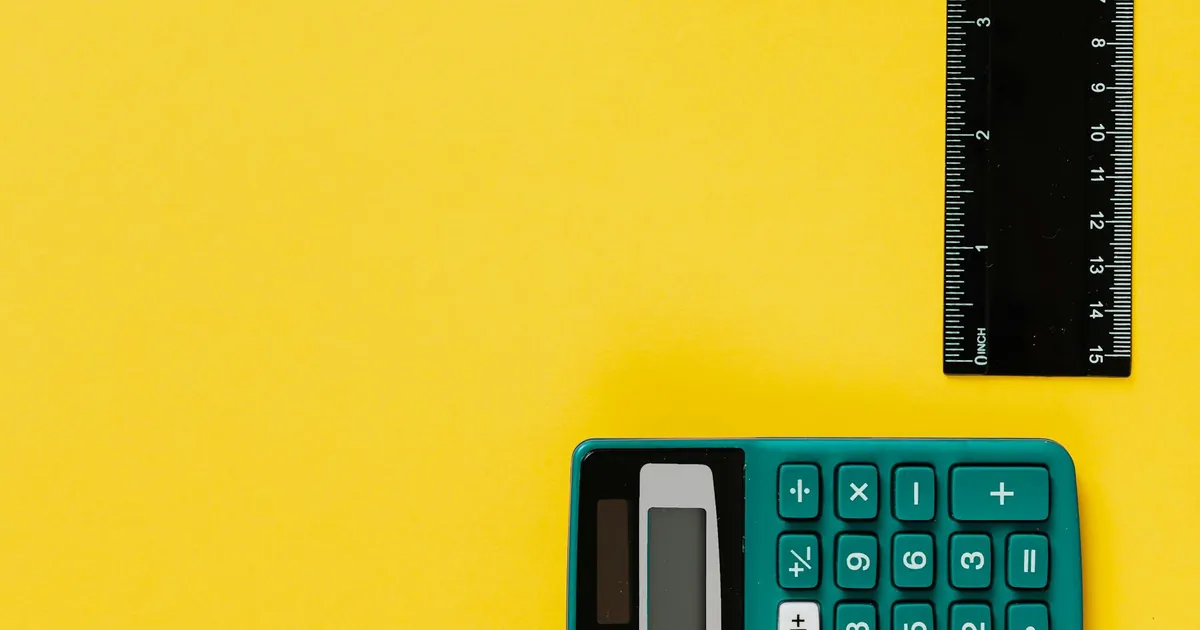 A bright teal calculator and black ruler on a vivid yellow surface. Ideal for educational themes.