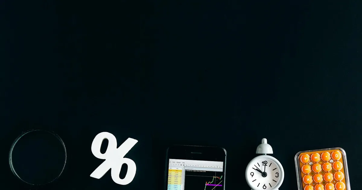Flat lay of financial analysis tools including phone, clock, and calculator on black background.