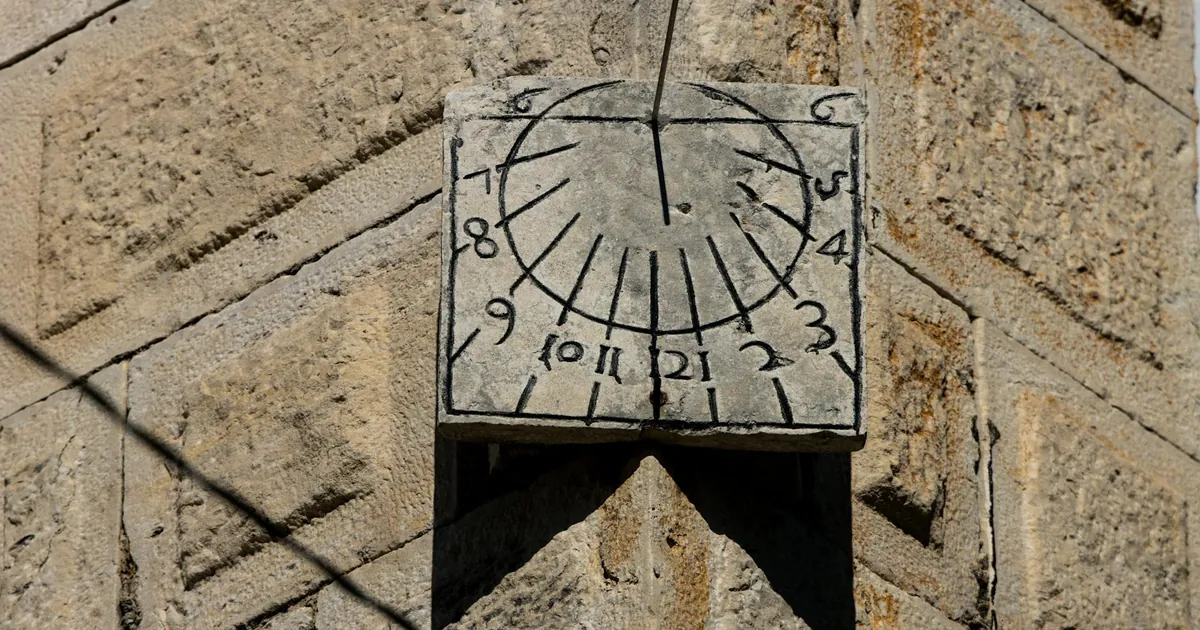 Close-up of a traditional stone sundial casting a shadow on an old stone wall. Close-up of a traditional stone sundial casting a shadow on an old stone wall.
