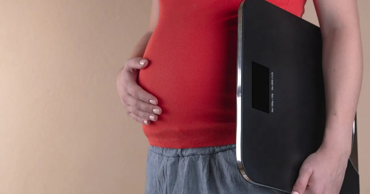 pregnant woman touching her belly and carrying a digital bathrooms cale