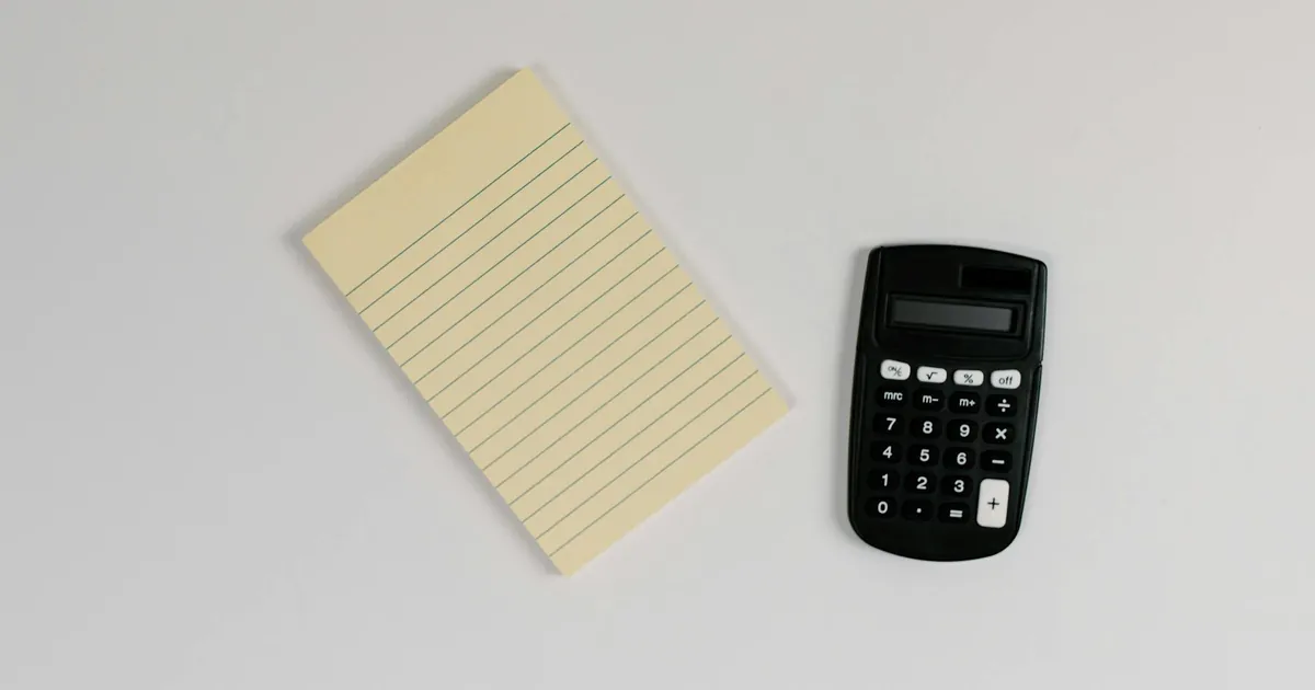 Top view of a minimalist setup with a yellow lined notepad and a black calculator on a white surface.