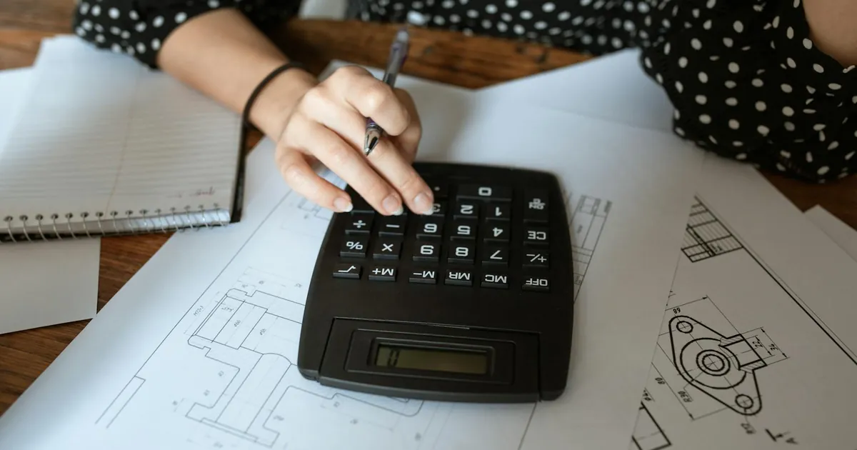 Close-up of an architect's hand using a calculator on technical drawings with a polka dot shirt.
