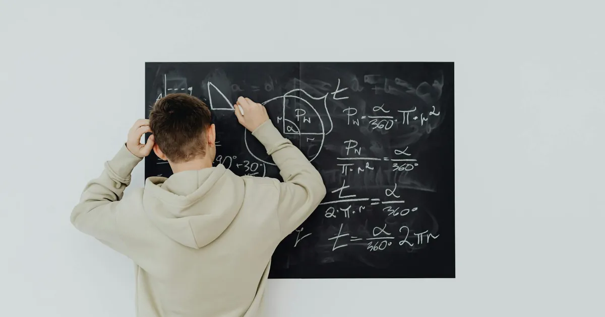 Teenager in hoodie writing math formulas on a blackboard indoors, showcasing problem-solving skills. Teenager in hoodie writing math formulas on a blackboard indoors, showcasing problem-solving skills.