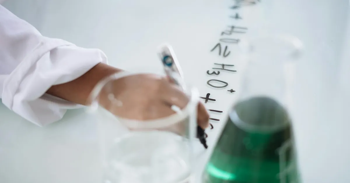 Body part of unrecognizable scientist in white uniform writing down formula after providing chemical research with fluid in flask during science lesson in university Body part of unrecognizable scientist in white uniform writing down formula after providing chemical research with fluid in flask during science lesson in university