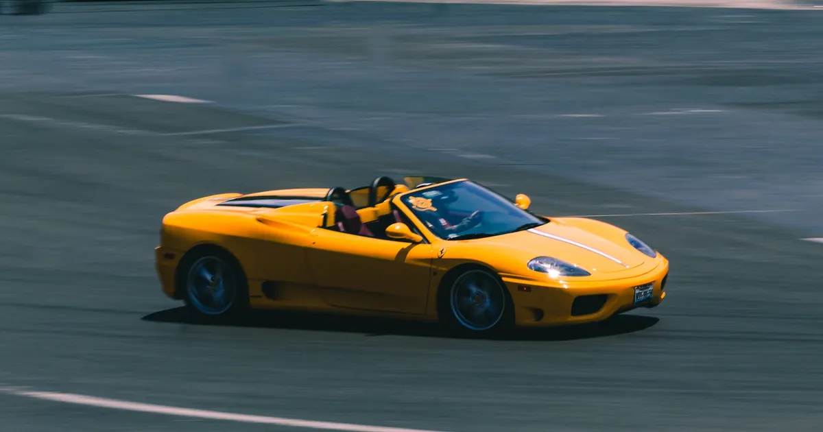 A vibrant yellow convertible sports car speeding on a racetrack, showcasing blurred motion and high speed.