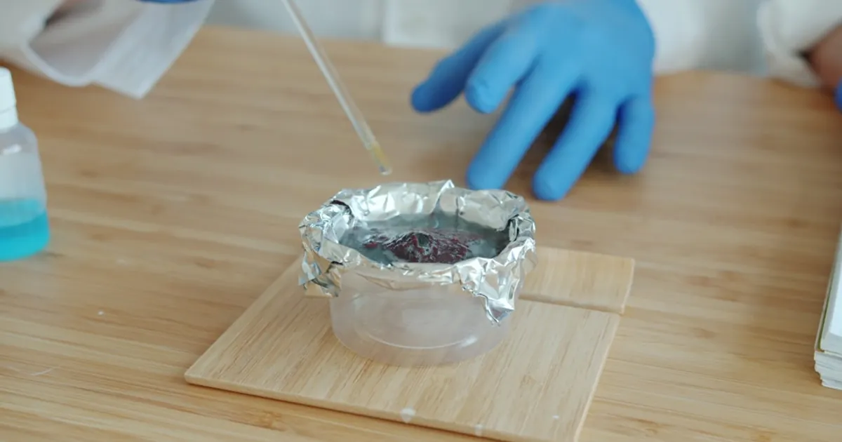 Scientist in blue gloves adding liquid to experiment
