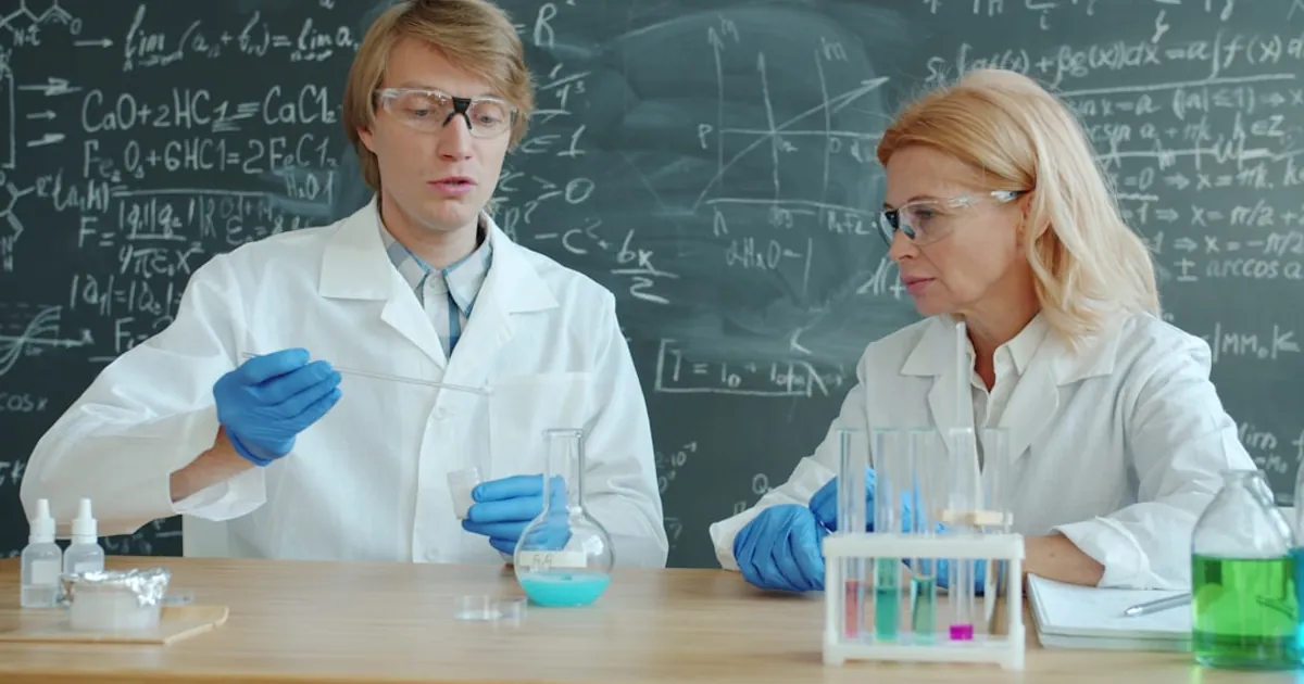 Two scientists in lab coats working with chemicals.