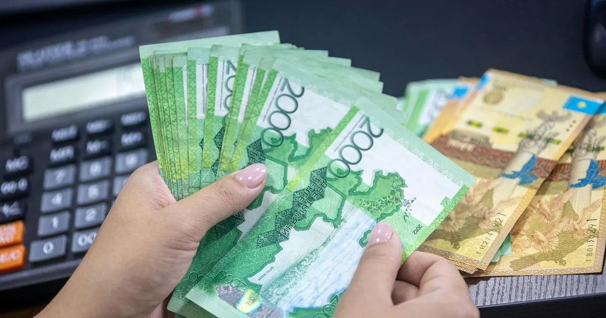Close-up of hands counting Kazakhstani Tenge notes on a desk with calculator.