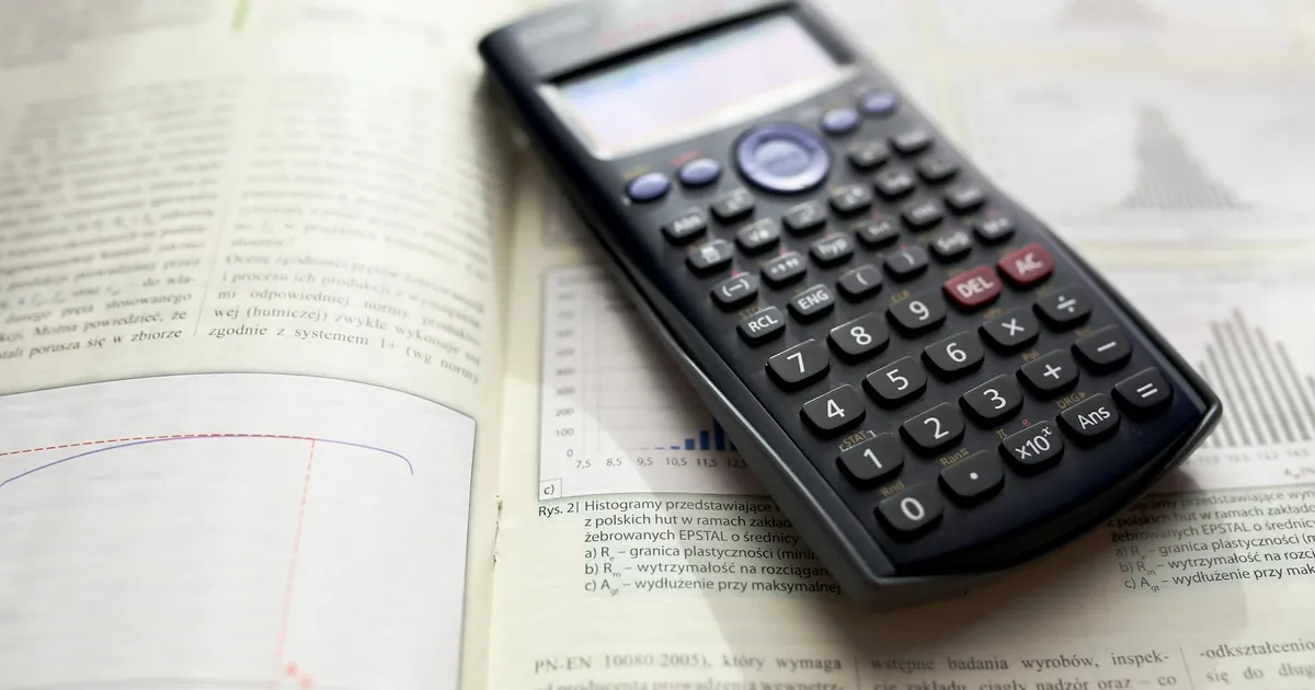 A graphing calculator rests on an open mathematics book with graphs and equations.
