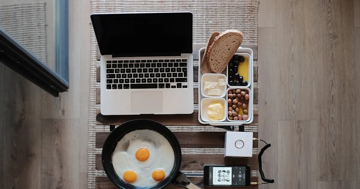 photo of MacBook Pro, frying pan with eggs and bread on gray mat