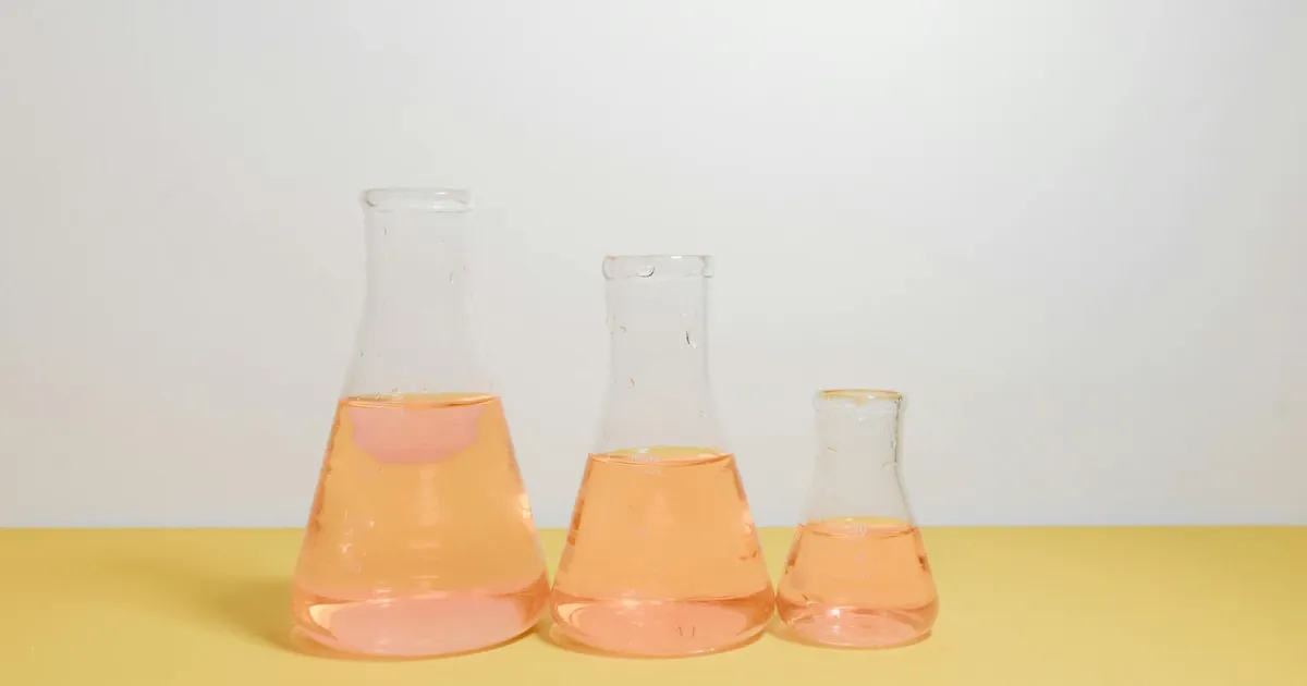 Three Erlenmeyer flasks filled with pink liquid on a yellow surface in a lab setting.