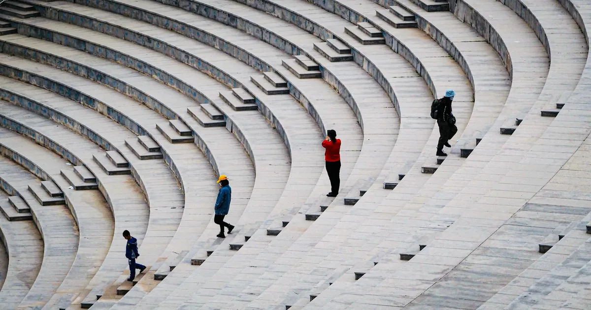 Aerial view of four people walking on curved amphitheater steps, creating a rhythmic pattern. Aerial view of four people walking on curved amphitheater steps, creating a rhythmic pattern.