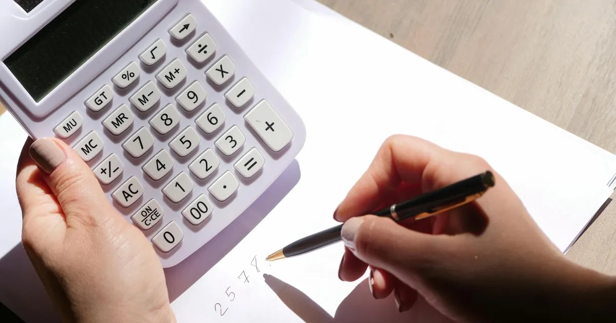 Hands using a calculator and writing numbers on paper under sunlight. Ideal for finance and education themes.