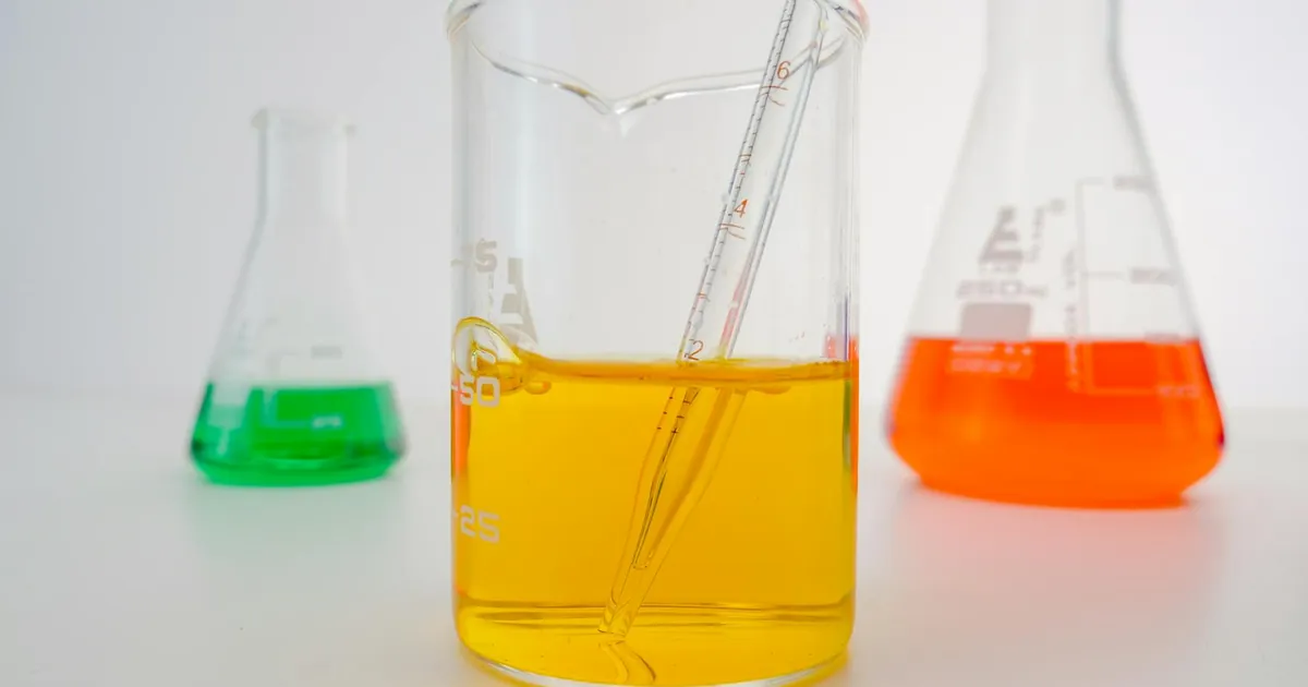 Close-up of vibrant chemical solutions in beakers with pipette in a lab setting.